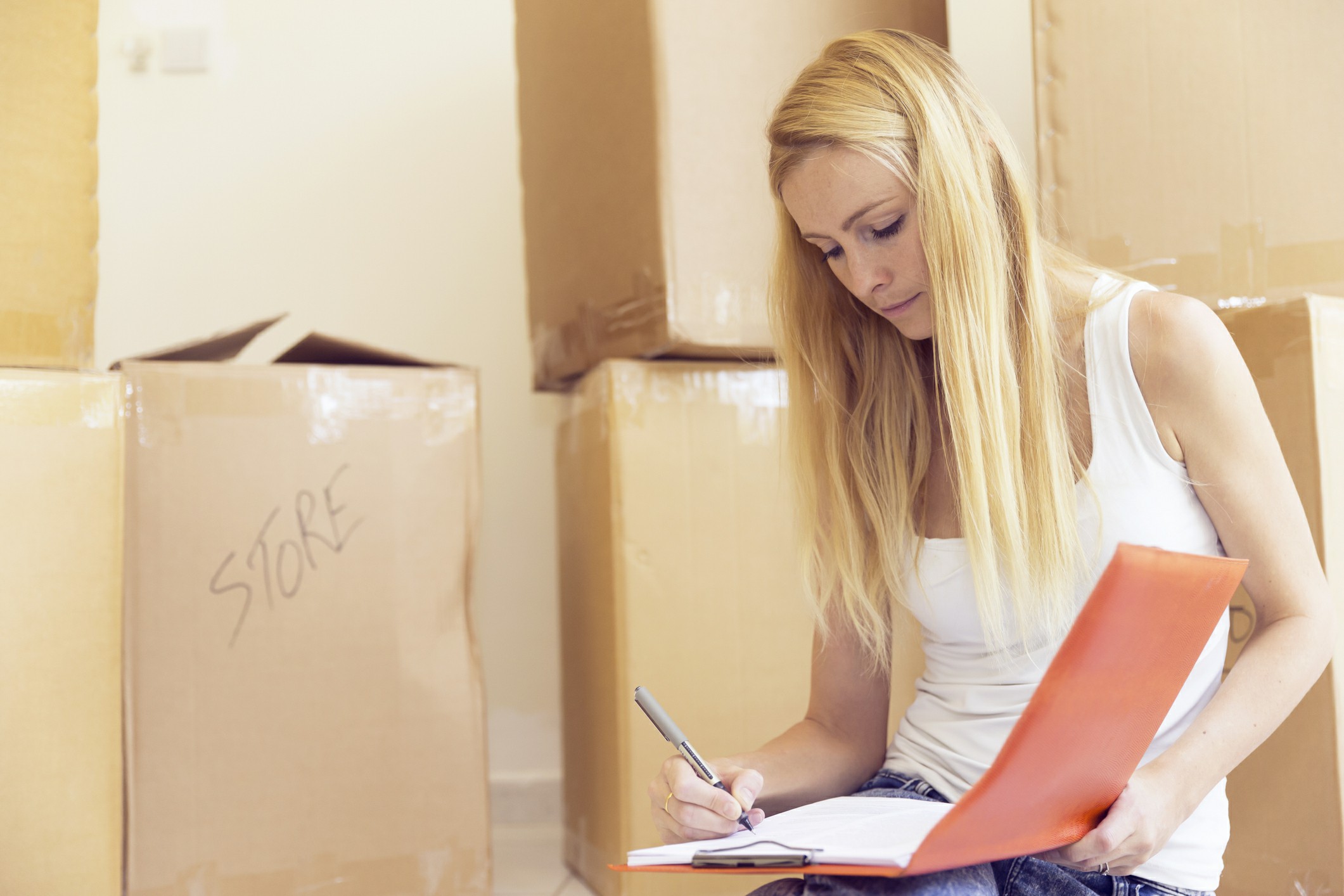 Woman preparing a moving checklist while surrounded by labeled cardboard boxes during home relocation with Chess Moving.