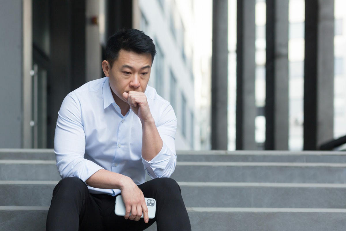 Tips for Managing Culture Shock and Easing the Transition An Asian man sits thoughtfully on steps, resting his chin on his hand, reflecting in a moment of contemplation.