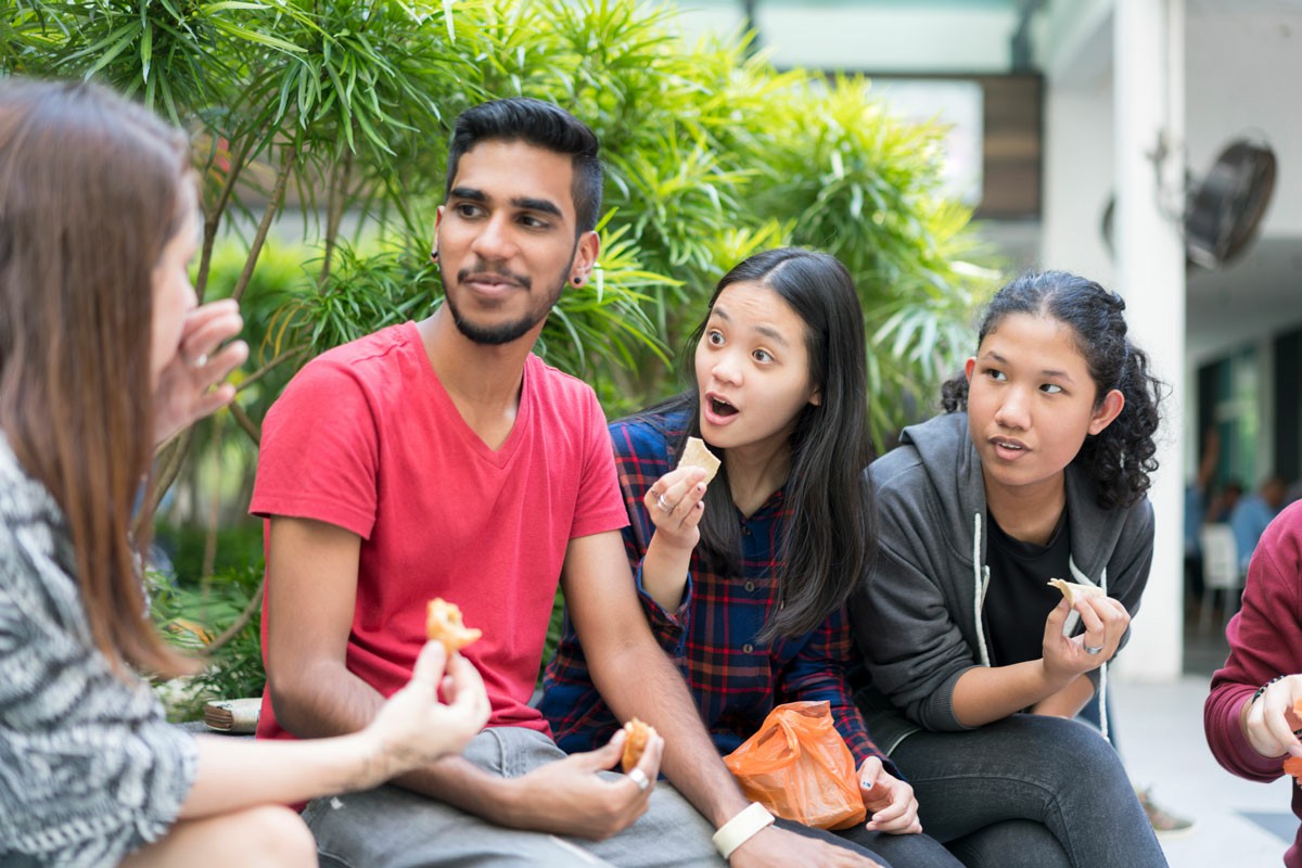 What is Culture Shock? A diverse group of young individuals enjoying a meal together outdoors, surrounded by greenery and a sunny atmosphere; What is culture shock
