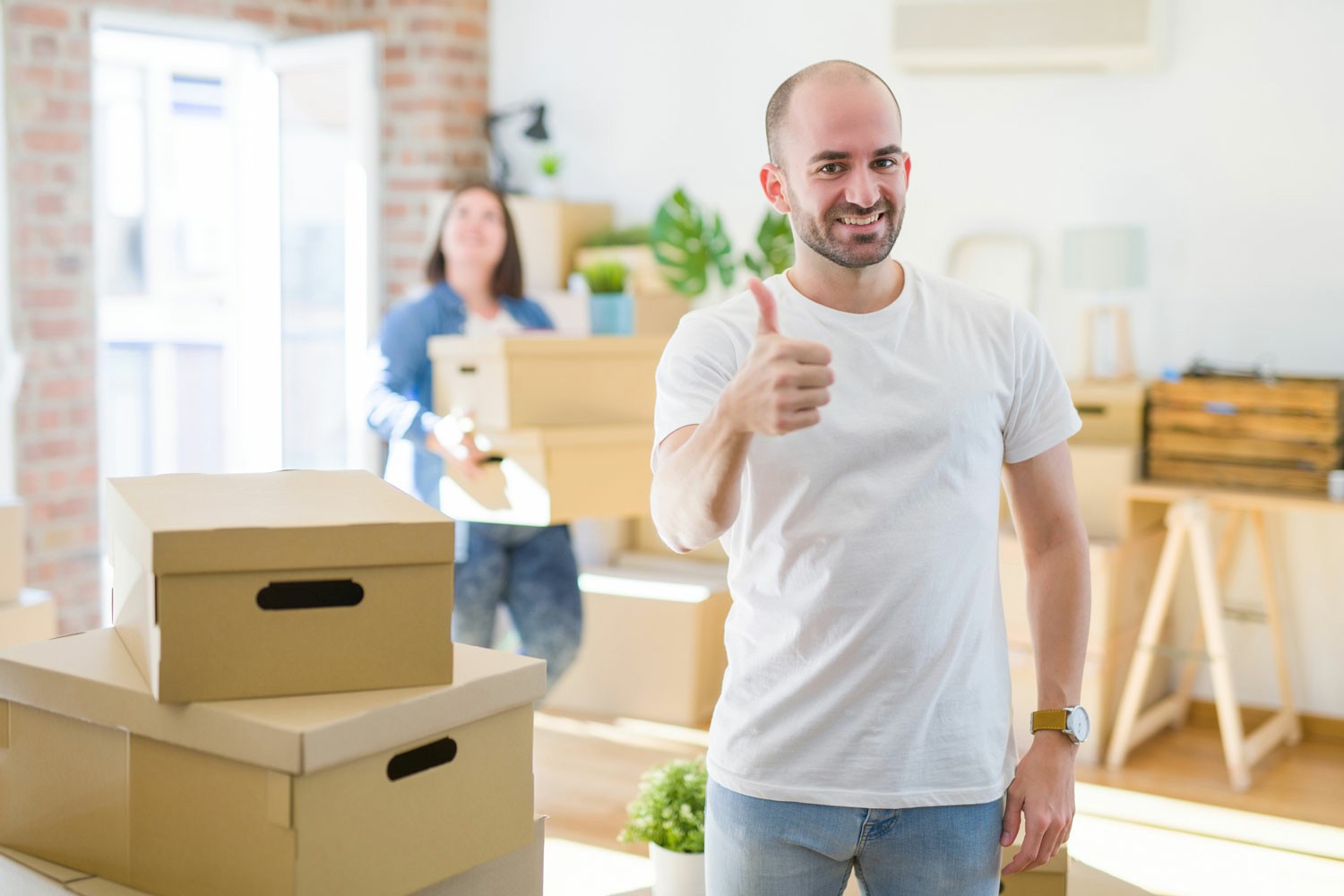 Faqs About Hiring a Moving Company A man and woman are positioned in a room surrounded by boxes, appearing to plan or organize their space. Faqs About Hiring a Moving Company