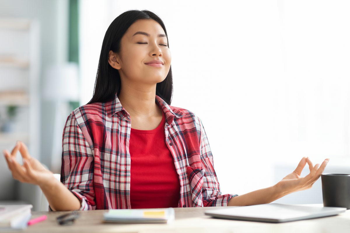 Taking Care of Yourself Managing Stress During The Process A woman sits cross-legged, meditating peacefully in front of an open laptop on a desk, surrounded by a calm atmosphere. Taking Care of Yourself Managing Stress During The Process
