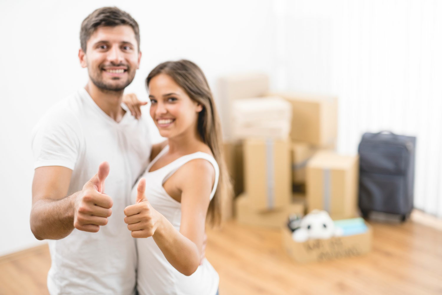The Benefits of Choosing A Professional Moving Company A couple stands in front of a moving box, both giving a thumbs up, smiling and celebrating their new adventure. The Benefits of Choosing A Professional Moving Company