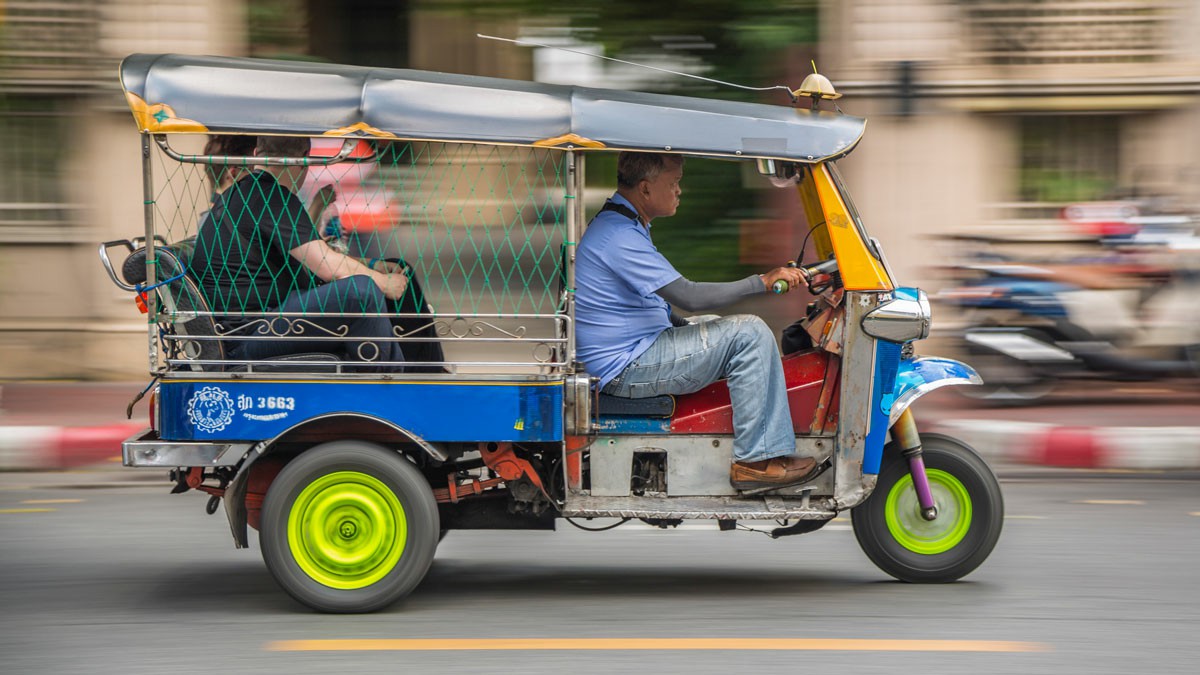 Getting Around in Thailand Transportation and Driving Tips A man operating a compact vehicle on a busy street, with urban scenery in the background. Getting Around in Thailand Transportation and Driving Tips