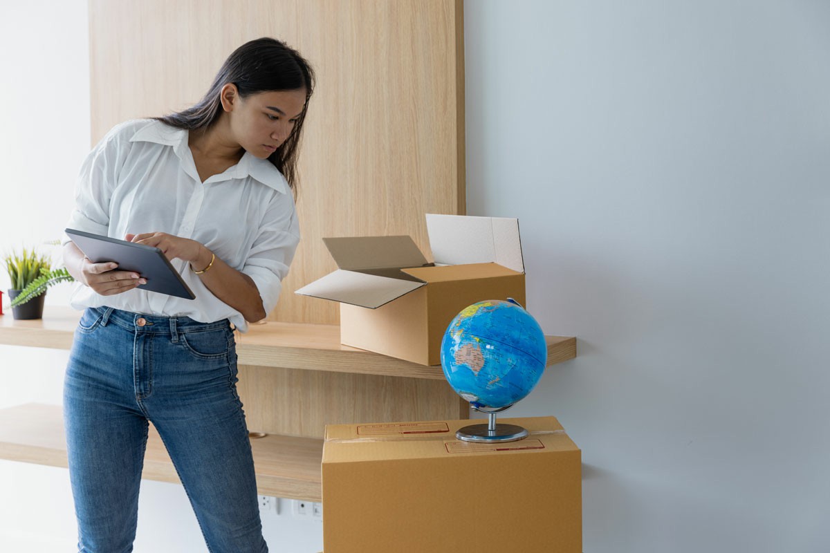 Essential Preparations Before Moving Overseas for Work Woman unpacking boxes and a globe in her new home, surrounded by moving supplies and a sense of new beginnings. Essential Preparations Before Moving Overseas for Work