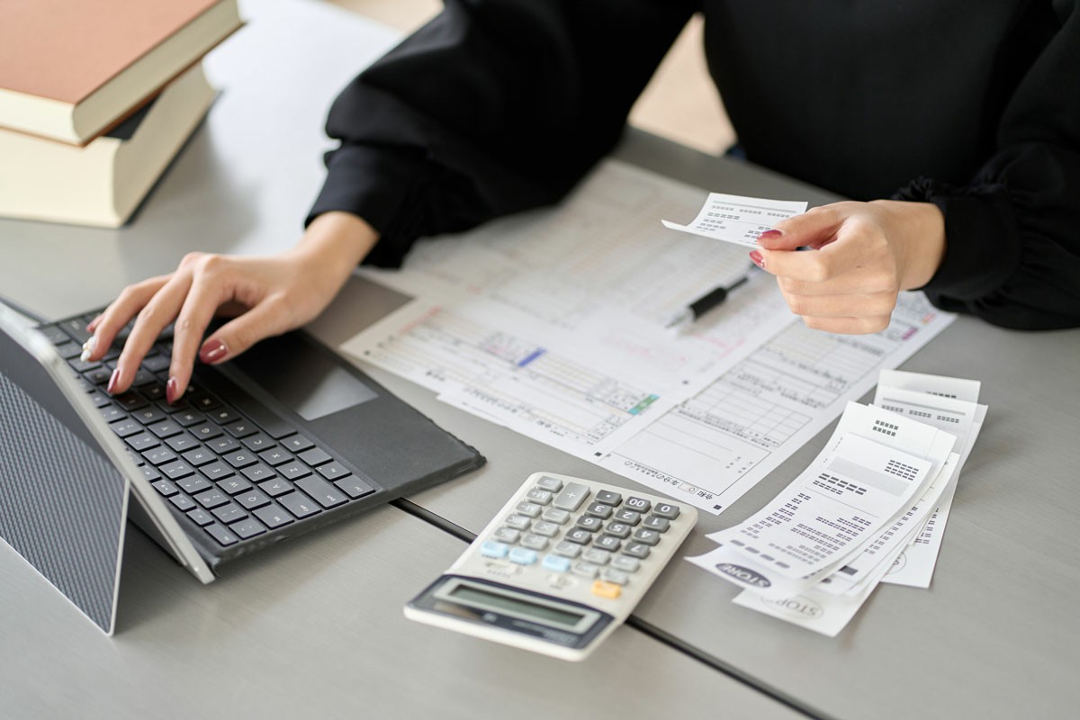 Managing Finances When Moving Overseas for Work A woman sits at a desk, using a laptop and calculator to manage and pay her bills. Managing Finances When Moving Overseas for Work
