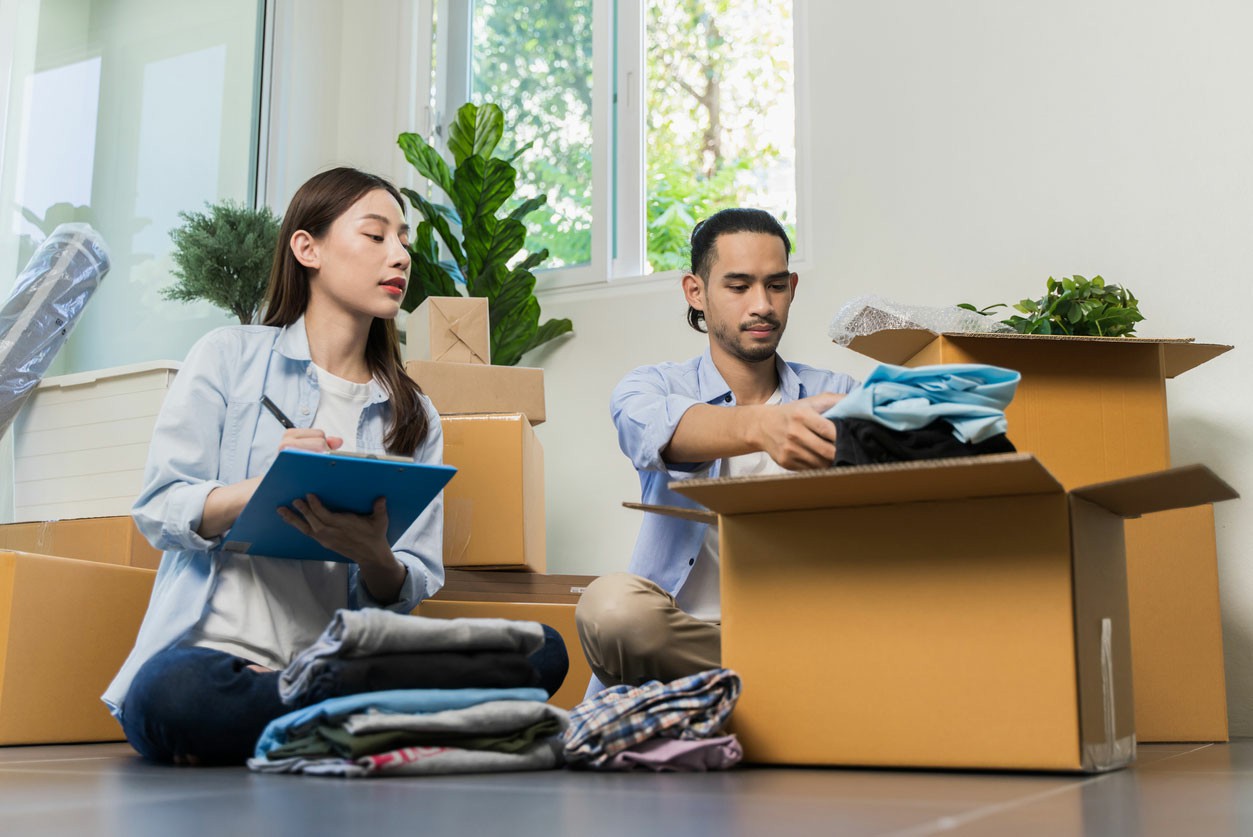  A man and woman sit on the floor surrounded by boxes and clothes, appearing to organize their belonging. Final Steps Booking and Preparing for Moving Day