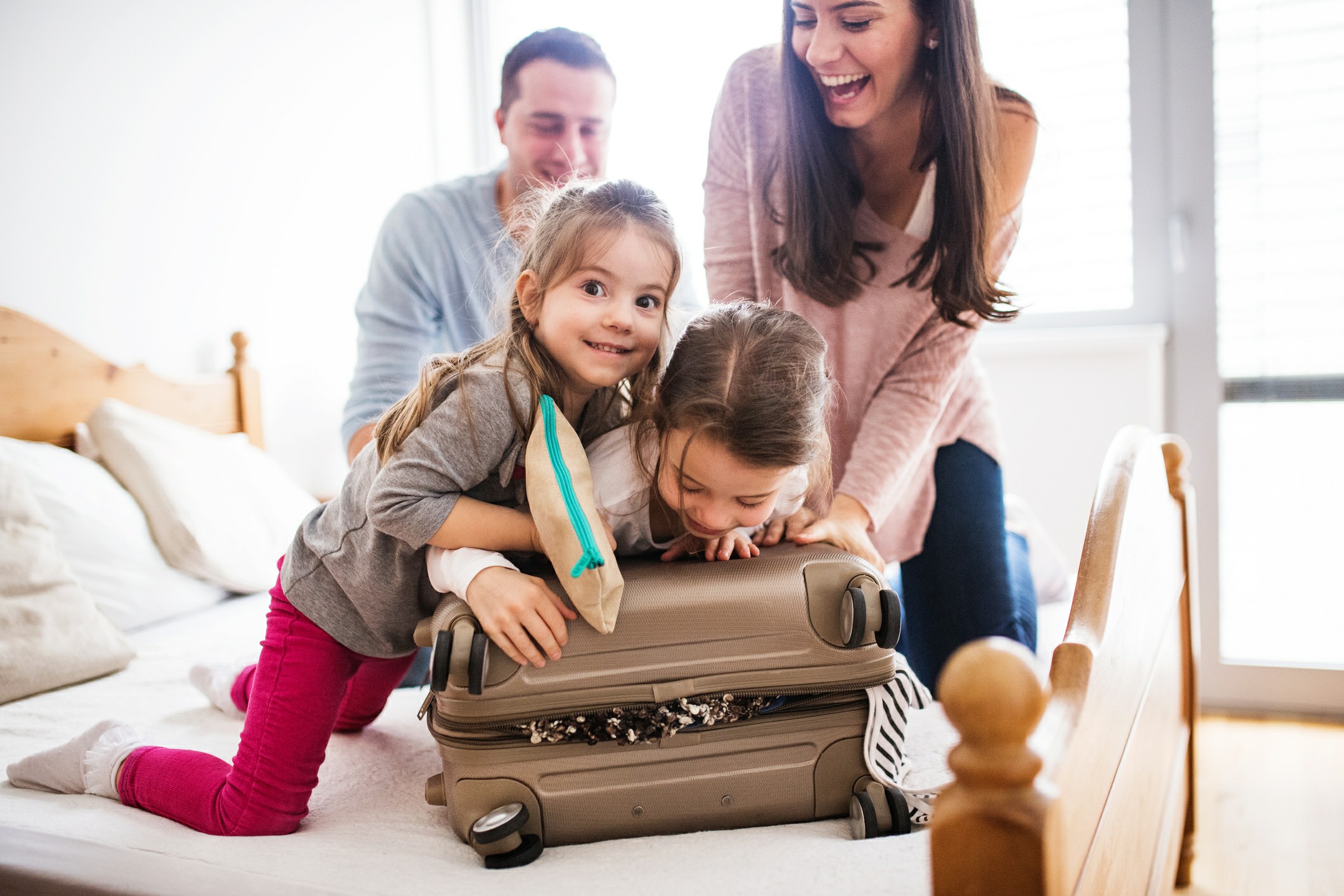 Kids laying on luggage to help close it with parents in the background